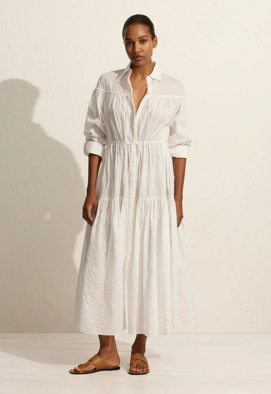 A voluminous maxi dress with traditional shirt details, including a concealed button placket and collar. Featuring an adjustable drawcord tie at the yoke and waist, and a relaxed fit sleeve with button cuffs. Made from organic cotton voile with linear embroidery.