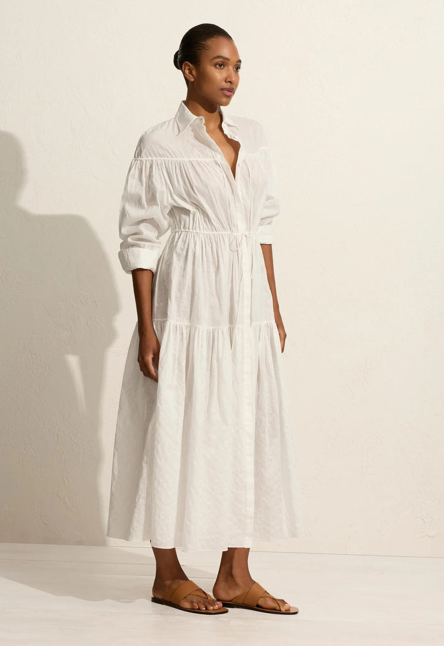 A voluminous maxi dress with traditional shirt details, including a concealed button placket and collar. Featuring an adjustable drawcord tie at the yoke and waist, and a relaxed fit sleeve with button cuffs. Made from organic cotton voile with linear embroidery.