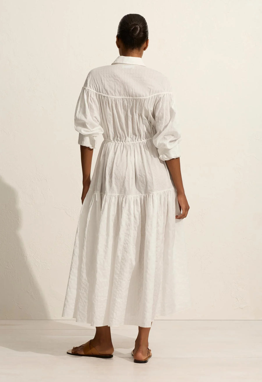A voluminous maxi dress with traditional shirt details, including a concealed button placket and collar. Featuring an adjustable drawcord tie at the yoke and waist, and a relaxed fit sleeve with button cuffs. Made from organic cotton voile with linear embroidery.