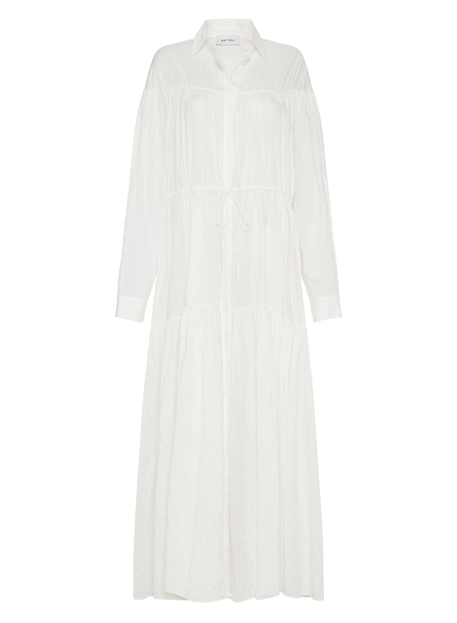 A voluminous maxi dress with traditional shirt details, including a concealed button placket and collar. Featuring an adjustable drawcord tie at the yoke and waist, and a relaxed fit sleeve with button cuffs. Made from organic cotton voile with linear embroidery.