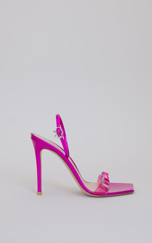 A squared-toe sandal with a stiletto heel. The ankle strap is embellished with a ribbon buckle and the front strap features see-through plexi with crystal gems.